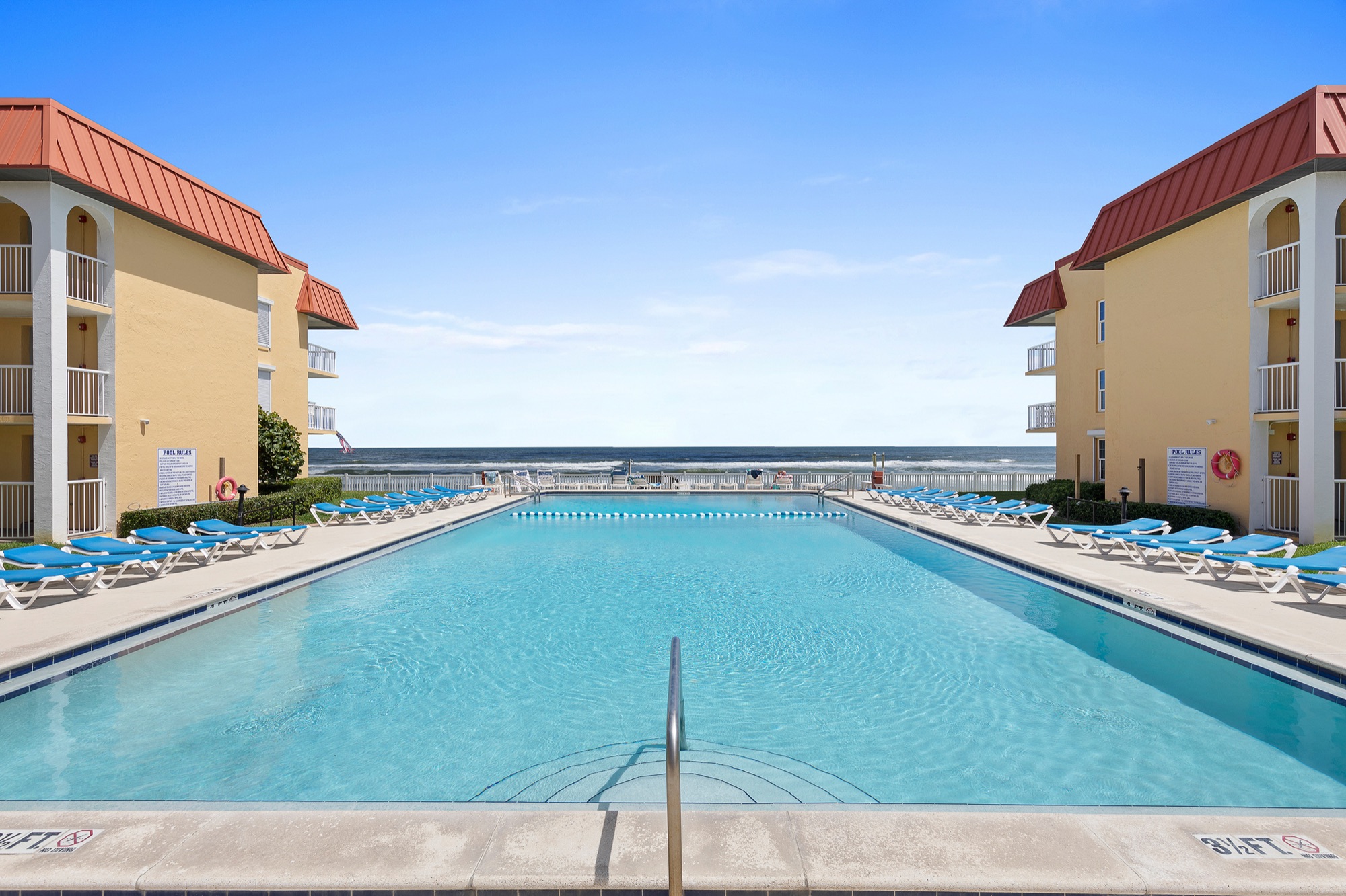 Oceanfront pool at Point East, flanked by yellow condo buildings with red roofs, with the Atlantic on the horizon