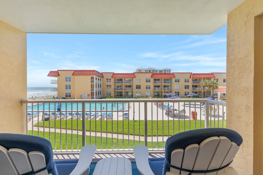 Covered balcony with navy Adirondack chairs overlooking the pool, lawn, and ocean