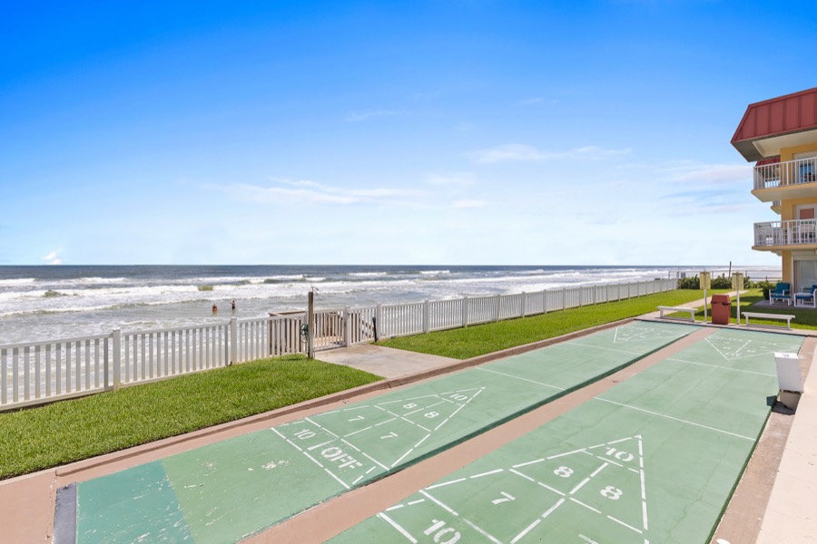 Oceanfront shuffleboard courts beside a white picket fence with waves beyond