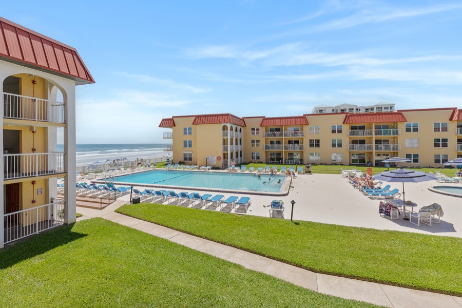 Elevated view of the yellow, red-roofed Point East complex and pool deck with the beach beyond
