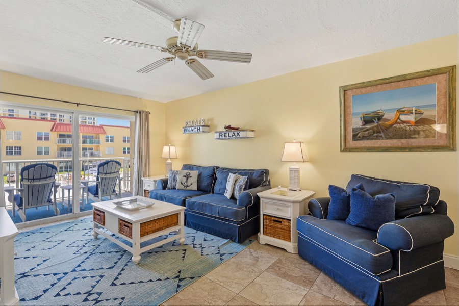 Living room with two blue sofas, beach artwork, and sliding doors to the balcony