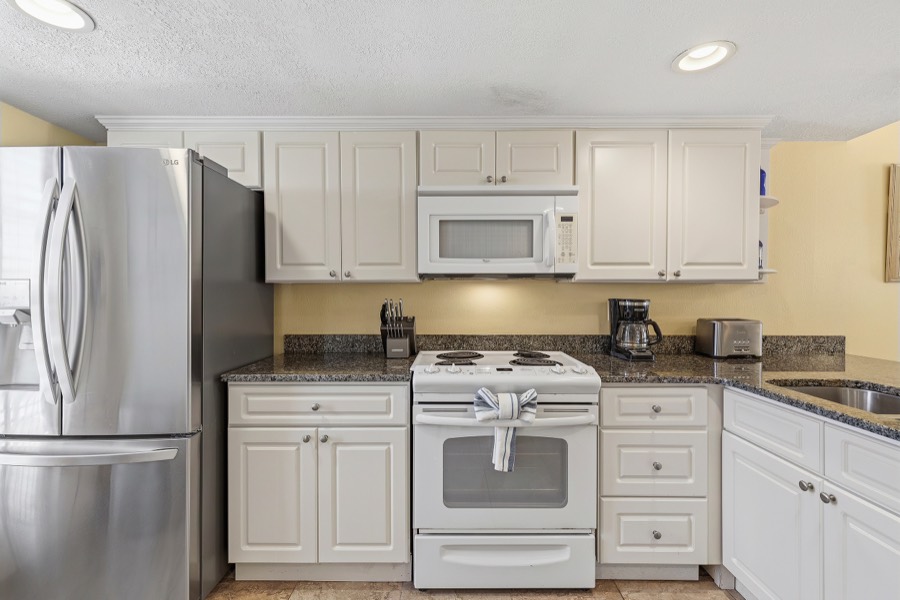 Kitchen with white cabinets, stainless refrigerator, microwave, and range