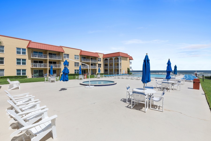 Pool deck with white Adirondack chairs and blue umbrellas