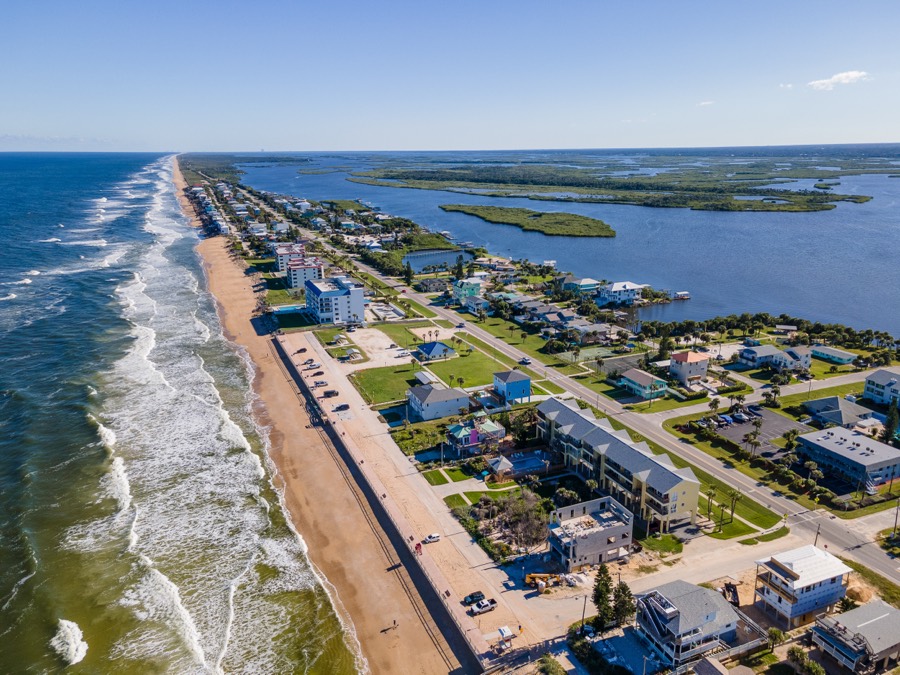 Aerial view of the New Smyrna Beach coastline with surf, wide sand, and the intracoastal waterway