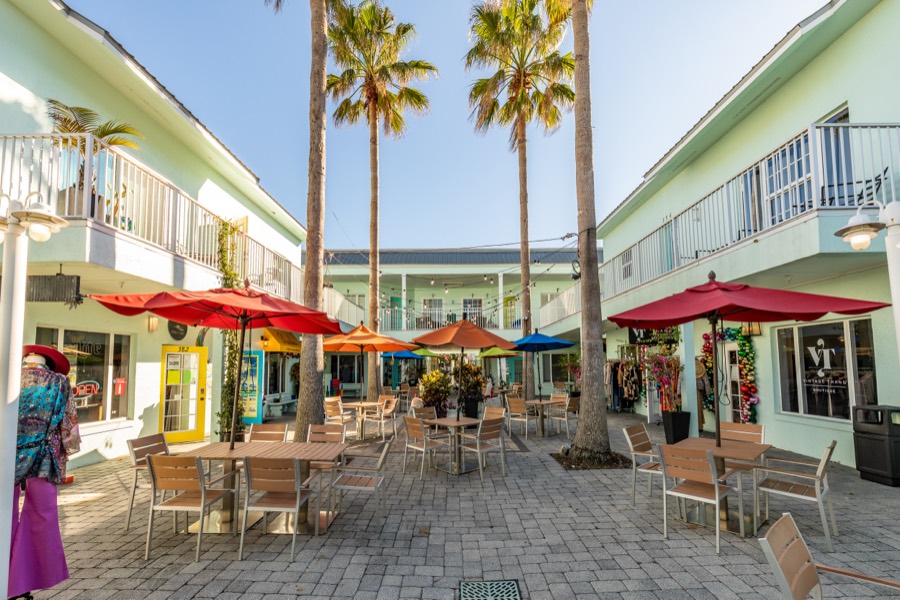 Palm-lined shopping courtyard with red umbrellas and cafe tables