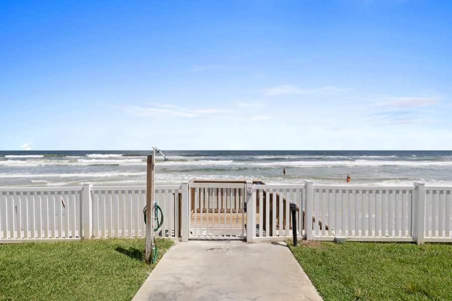 Gated beach walkway through a white picket fence leading onto the sand