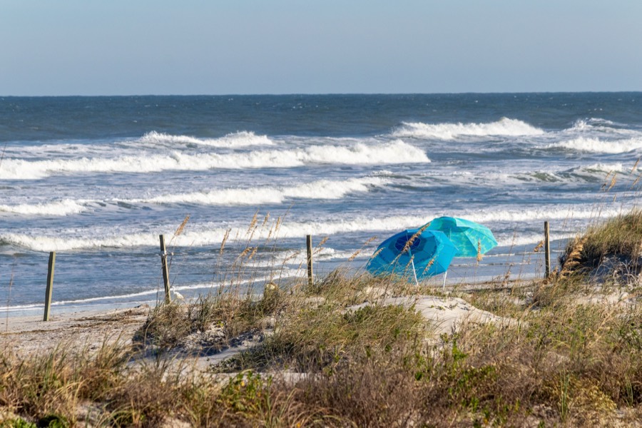 Turquoise beach umbrella among dune grasses with waves breaking offshore