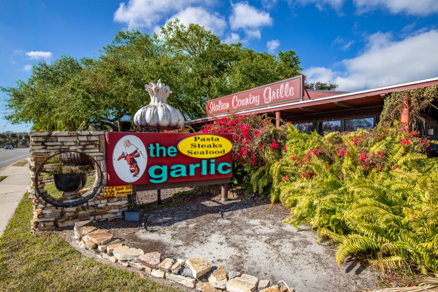 Roadside sign for The Garlic Italian Country Grille framed by bougainvillea